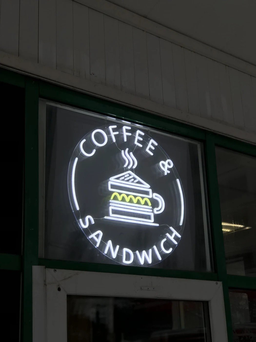Белая круглая неоновая надпись COFFEE & SANDWICH над входом
