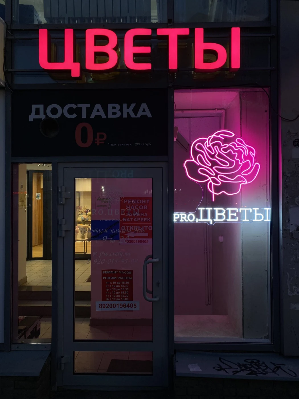 Красная неоновая надпись ЦВЕТЫ и розовый световой рисунок розы у входа
