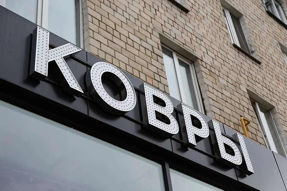 Белые объёмные буквы КОВРЫ на кирпичном фасаде здания