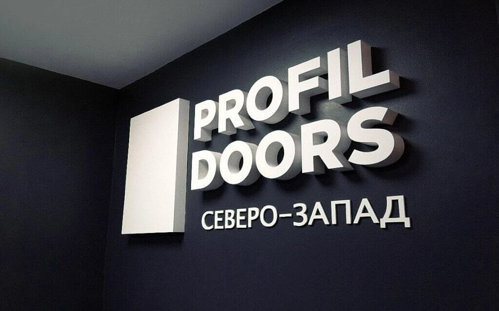 Белые объёмные буквы PROFIL DOORS на тёмной стене