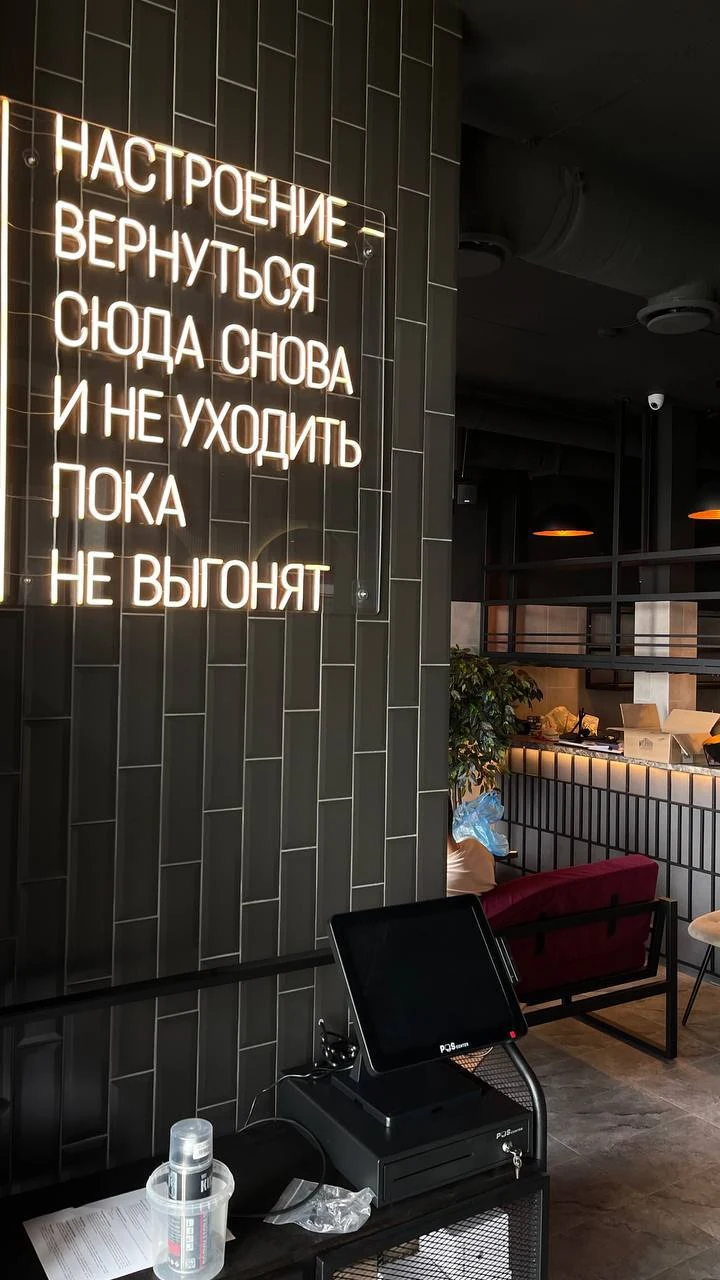 Тёплая неоновая фраза на тёмной плитке в интерьере кафе