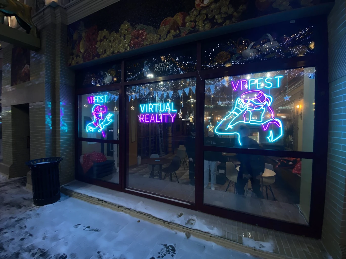 Синие и розовые неоновые надписи VR FEST в окнах помещения, вид с улицы