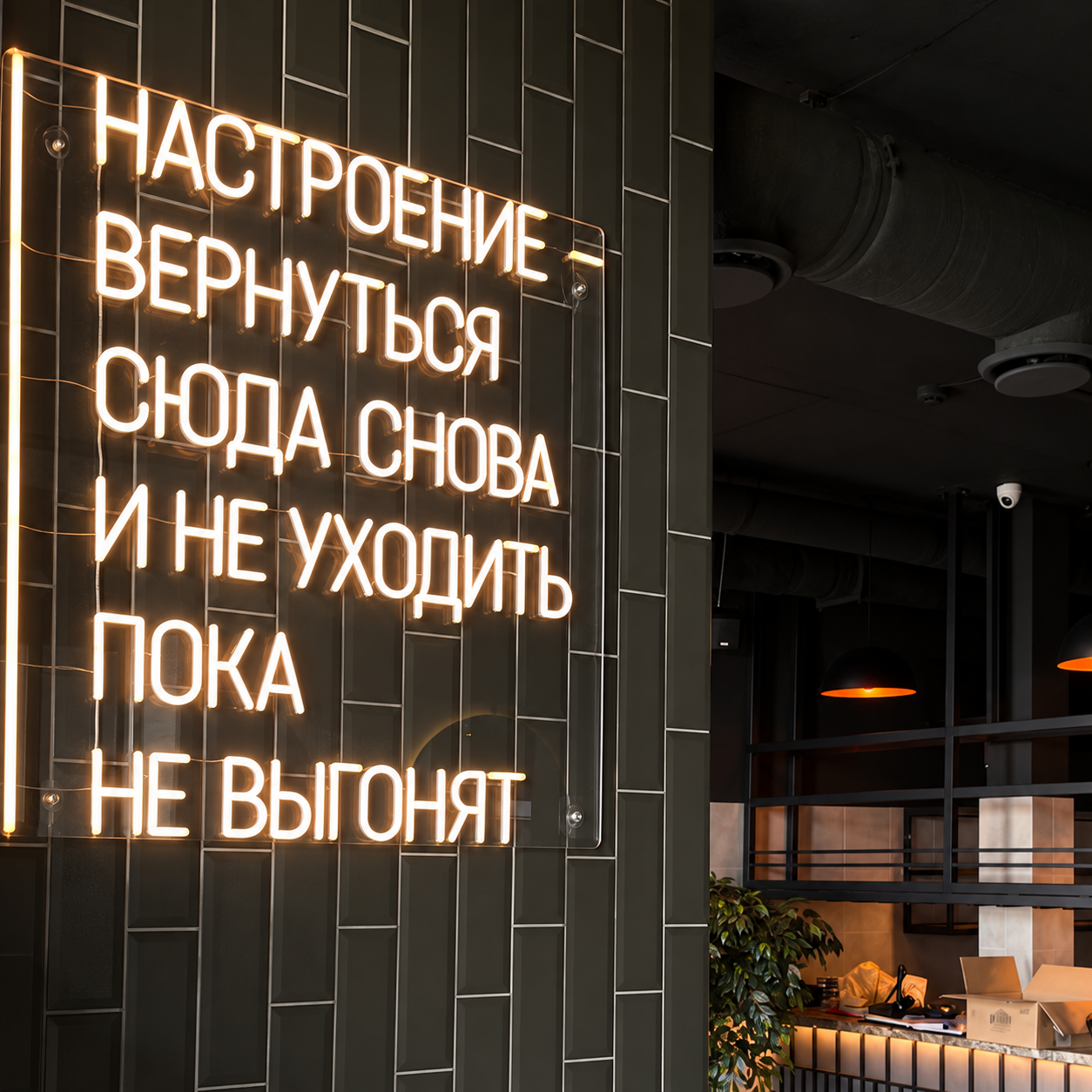 Тёплая белая неоновая надпись «Настроение — вернуться сюда снова и не уходить, пока не выгонят» на тёмной плиточной стене кафе. Визуализация на основе исходного фото.